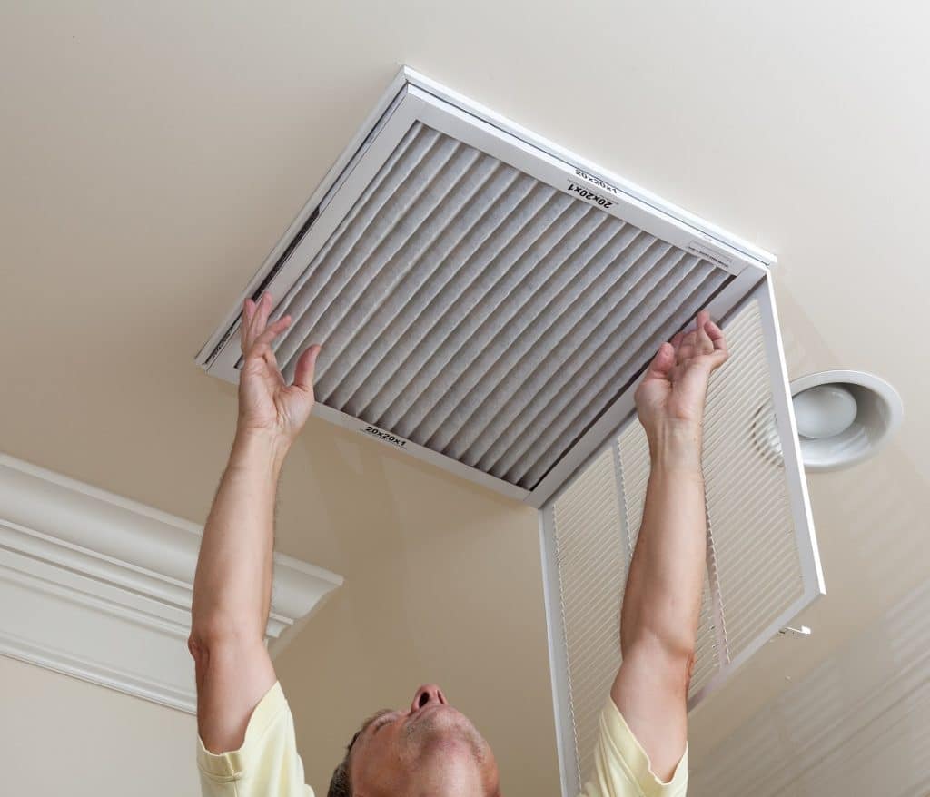 Senior male reaching up to open filter holder for air conditioning filter in ceiling