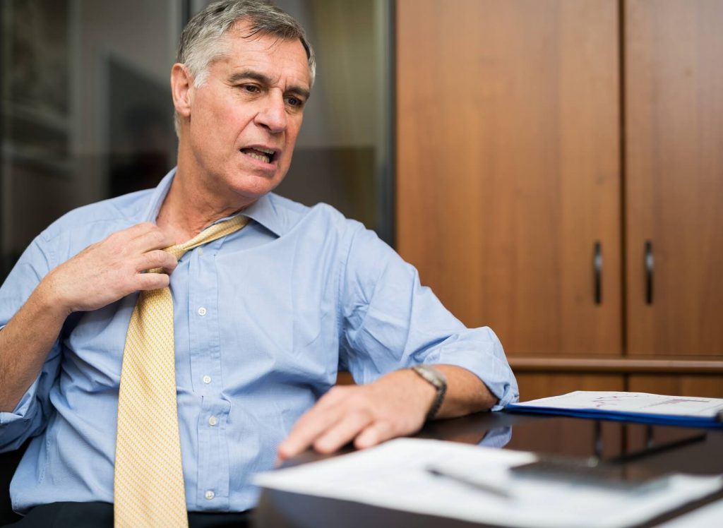 Man pulling on his tie in a hot office where the commercial HVAC stopped working 